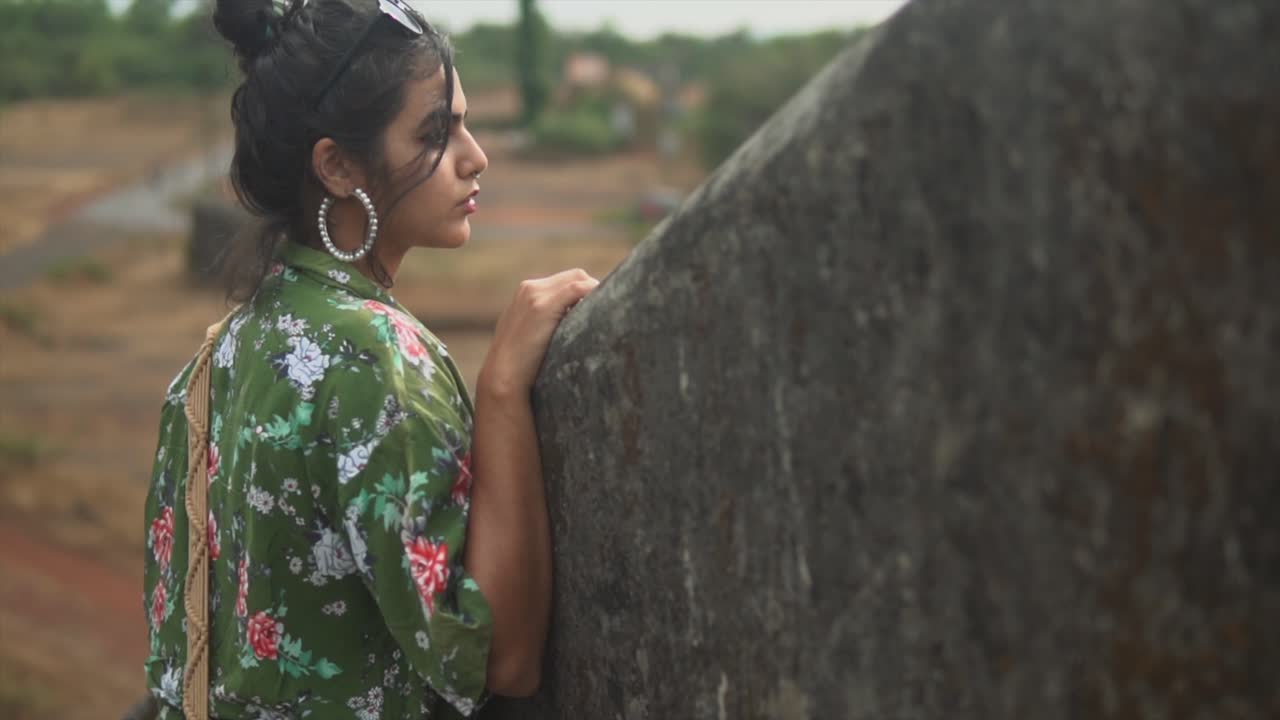 señorita con un pantalones verde estampado floral y pantalones blancos con el pelo oscuro mirando una granja en la india