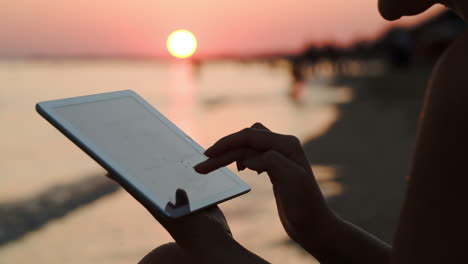 chica trabajando con una tableta en la playa al atardecer