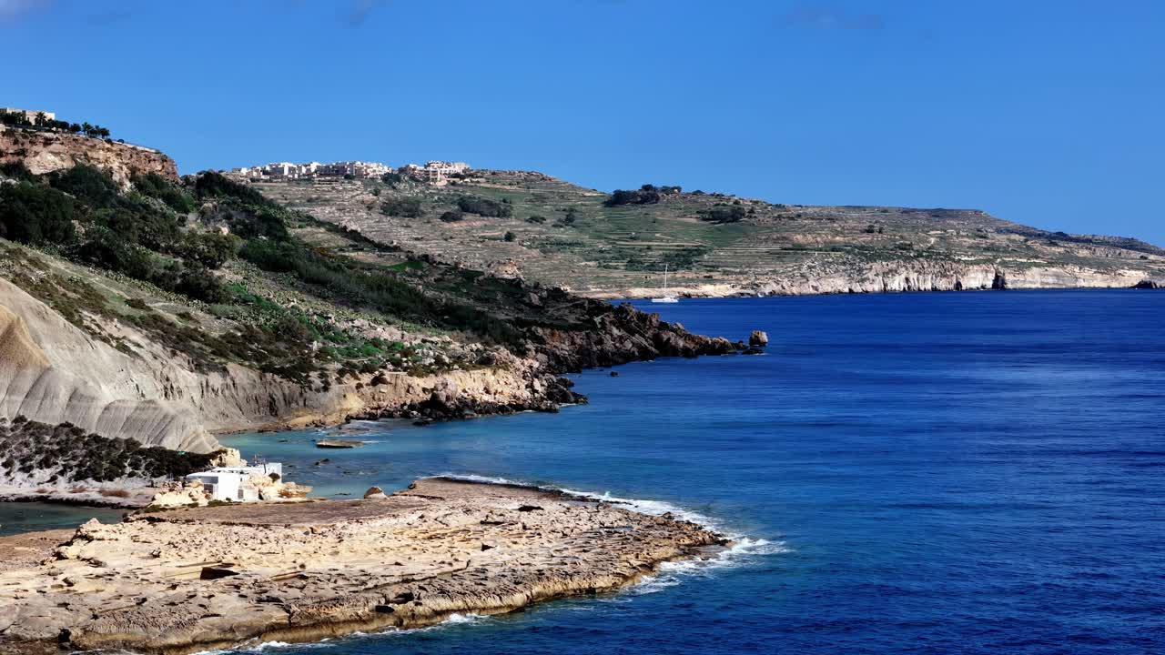 Ce magnifique plan grand-angle capture les falaises de calcaire escarpées de la côte maltaise sous un soleil d'été éclatant, où les eaux turquoises rencontrent les rivages rocheux dorés des îles de Gozo et Comino
