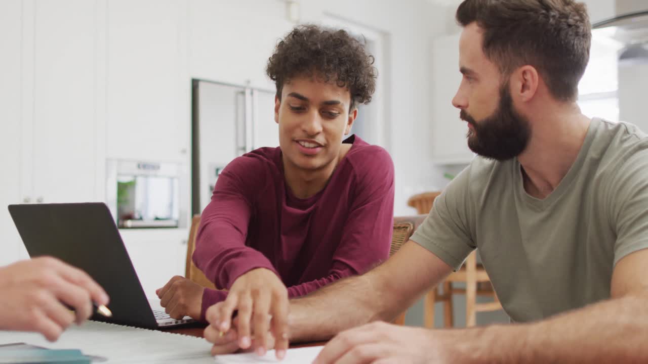 Happy diverse male friends talking and using laptop in living room