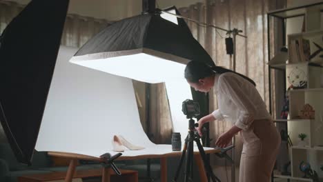 asian female photographer changing camera's lens while taking photos of women's shoes in home studio