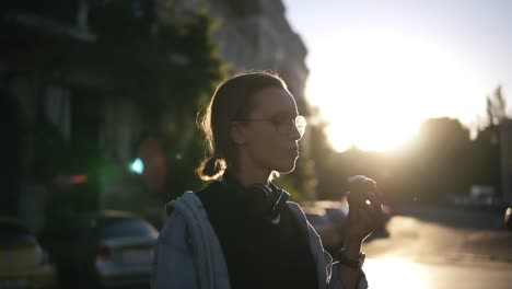 a girl in stylish glasses eats ice cream in a waffle cone in the rays of sunset. casual clothes. walking in the city. side view