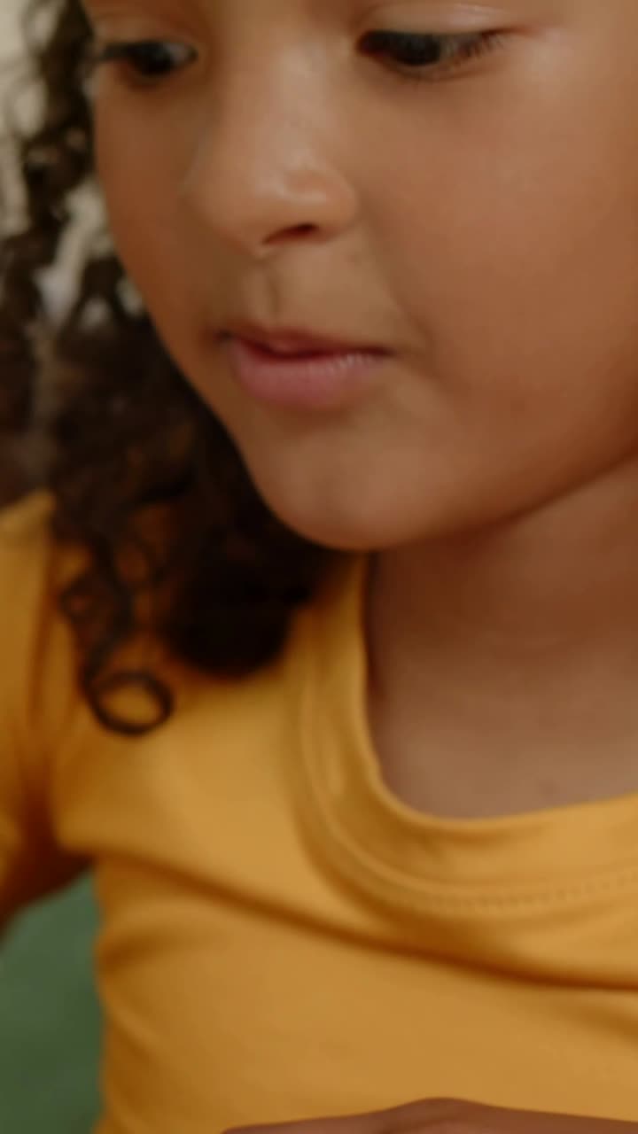 Vertical video: Reading girl in mustard tee looking down on couch, hand entering on table, cushion