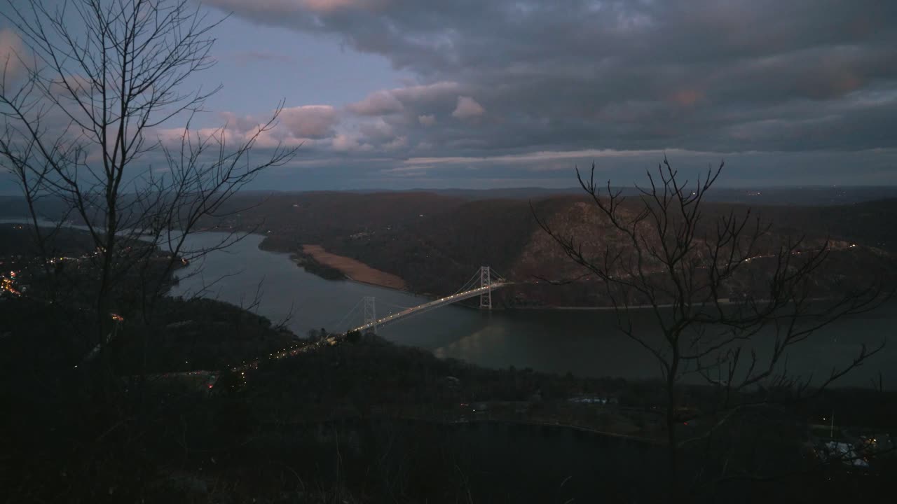 뉴욕 북부의 하드슨 강을 가로질러 산 꼭대기에서 밤에 다리를 건너고 있습니다.