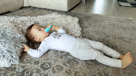relaxed little baby boy lies on the floor near the fluffy plaid. little kid holds a pacifier in mouth and waves his feet.