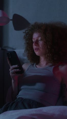 woman using phone in bed at night