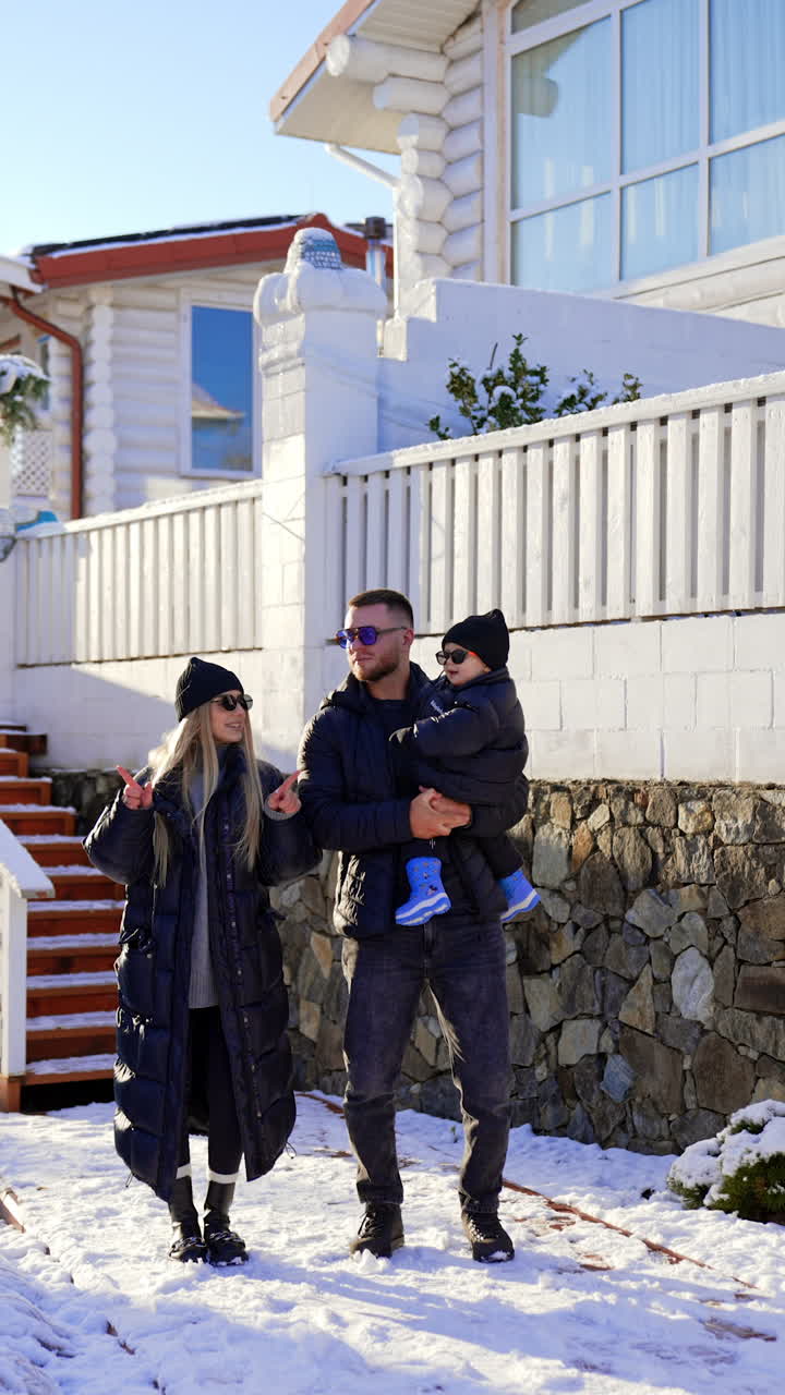 Cheerful Caucasian family wearing warm winter clothes stand outdoors. Couple and baby dance happily near their house. Vertical video.