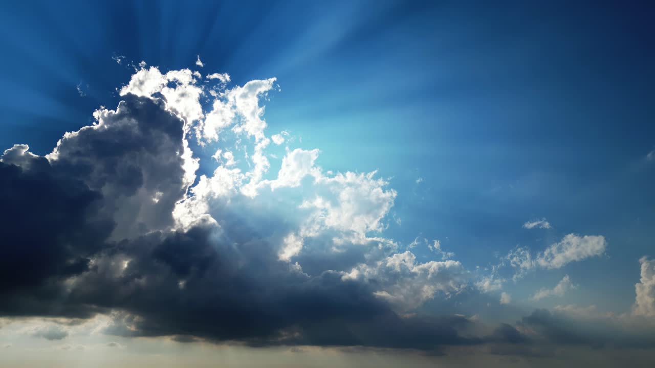 Nuvole cinematografiche che si muovono lentamente nel cielo con drammatici raggi di sole che filtrano attraverso formazioni scure contro un cielo diurno di un blu intenso.