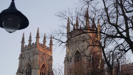 tight rising shot fo the two towers of huge english cathedral during an orange sunrise with lamp post in foreground