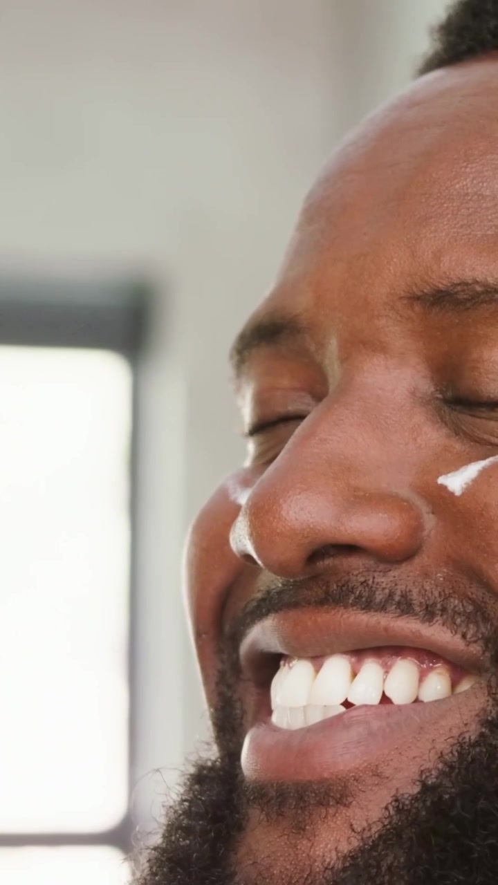 Vertical video: Seeing cream dab, man with beard applying cream with fingers by window for skincare