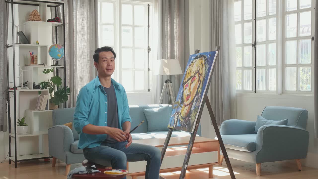 Asian Artist Man Sitting On Round Wooden Chair Without Backrest Holding Paintbrush Mixed Colour Wipe The Sweat Before Crossing His Arms And Smiling After Finish Painting A Girl On The Canvas