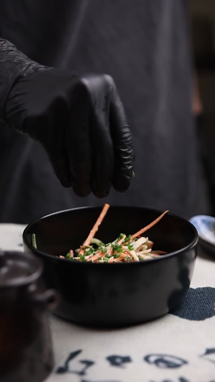 Mano con guanto nero che cosparge erbe fresche sull'insalata