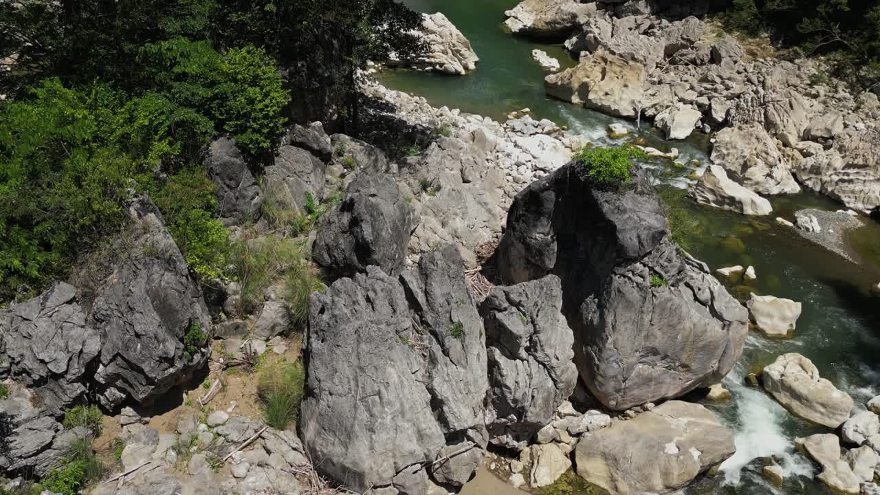 Medium-speed shot starts low showing flowing river passing large rocks, then rises to reveal the full river and surrounding landscape at Tinipak River, Philippines