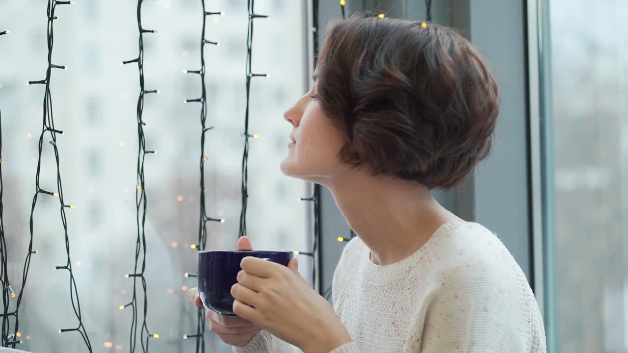 Woman enjoying a warm drink by the window during winter