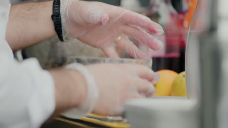 bartender placing ice cubes into crystal glasses at a bar, with fruits in the background