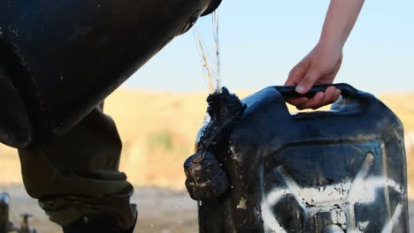 a soldier pours water to fill a black water tank with another soldier holding it in his hand