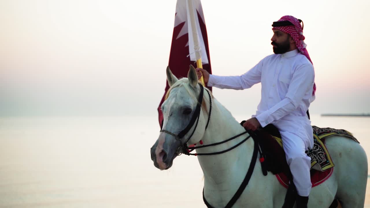 un caballero a caballo sosteniendo la bandera de qatar cerca del mar