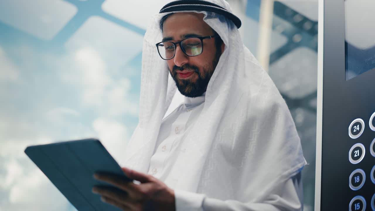 un hombre de negocios musulmán exitoso en el tradicional kandura blanco montando un ascensor de vidrio a la oficina en un centro de negocios moderno. un hombre usando una tableta.
