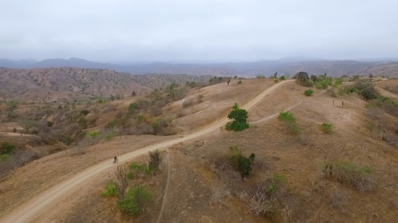 Ciclista en un camino de tierra con bicicleta de montaña descendiendo muy rápido en las colinas desérticas de Ecuador - Toma de dron - 50 fps.
