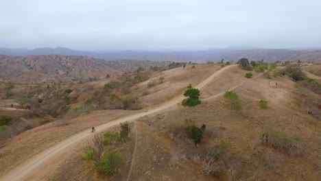 cyclist on a dirt road with mountain bike riding downhill very fast in desert hills of equador - drone shot - 50fps