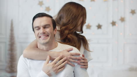 Smiling-wife-covering-her-husband-eyes-in-living-room