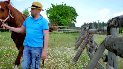 attractive man in hat walking with horse on the meadow