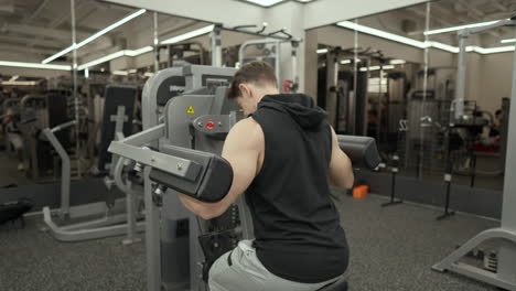 fit man with muscular arms workout in shoulder raise machine - back view