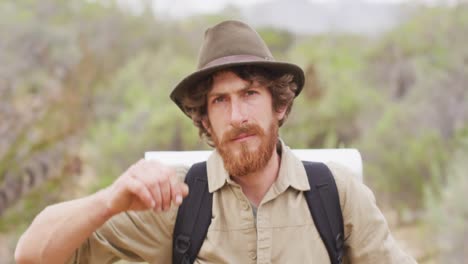 retrato de un hombre caucásico de supervivencia con barba, caminando por el desierto, levantando el sombrero.