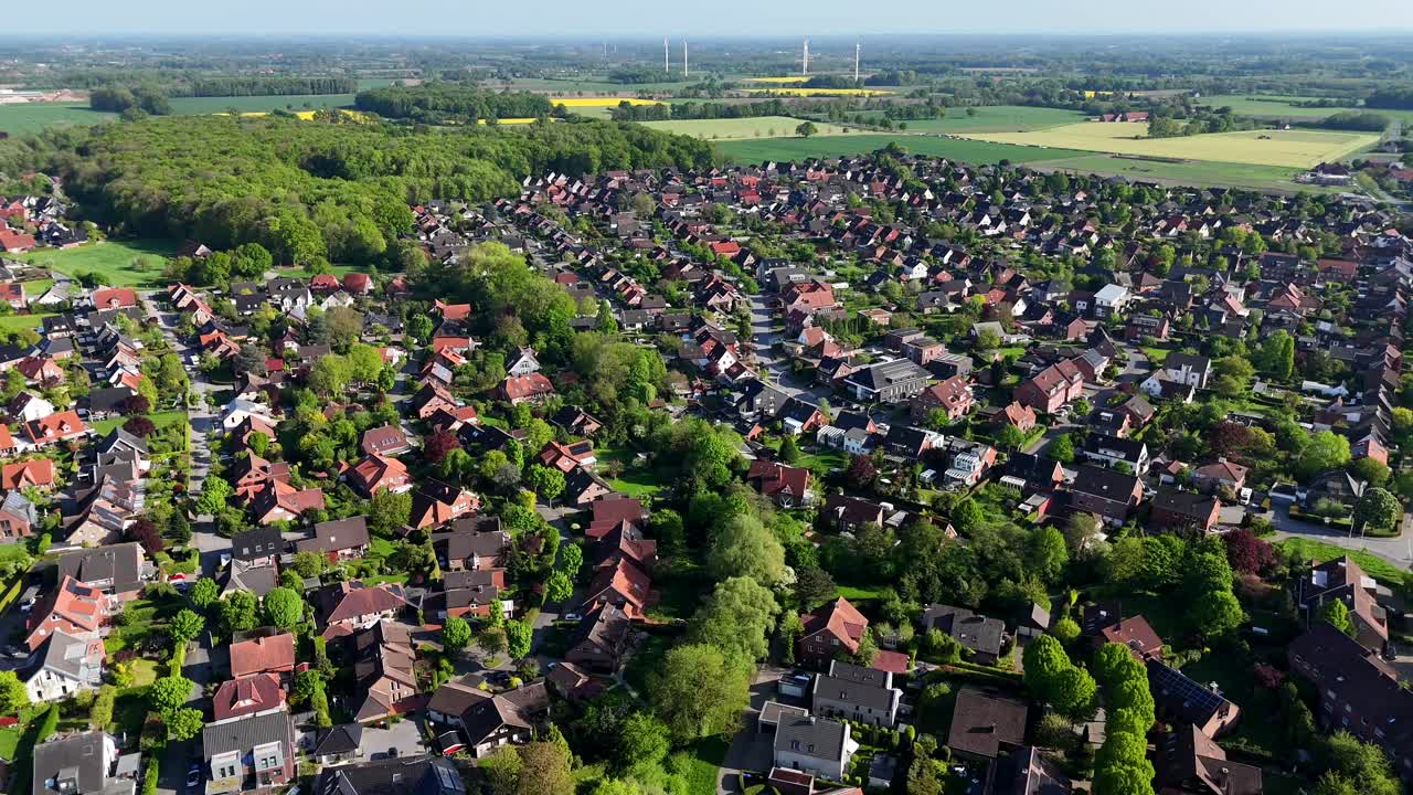 Green tree avenue in small american town during sunny day. Aerial wide shot. Modern wind turbines on farm fields in distance. Red roofs of houses and homes in peaceful neighborhood. Forest in back.