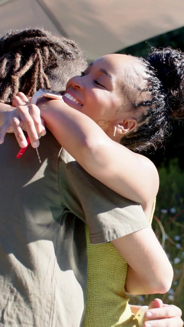 Vertical video: Wrapping woman in yellow hugging man, showing affection in yard and holding red fob