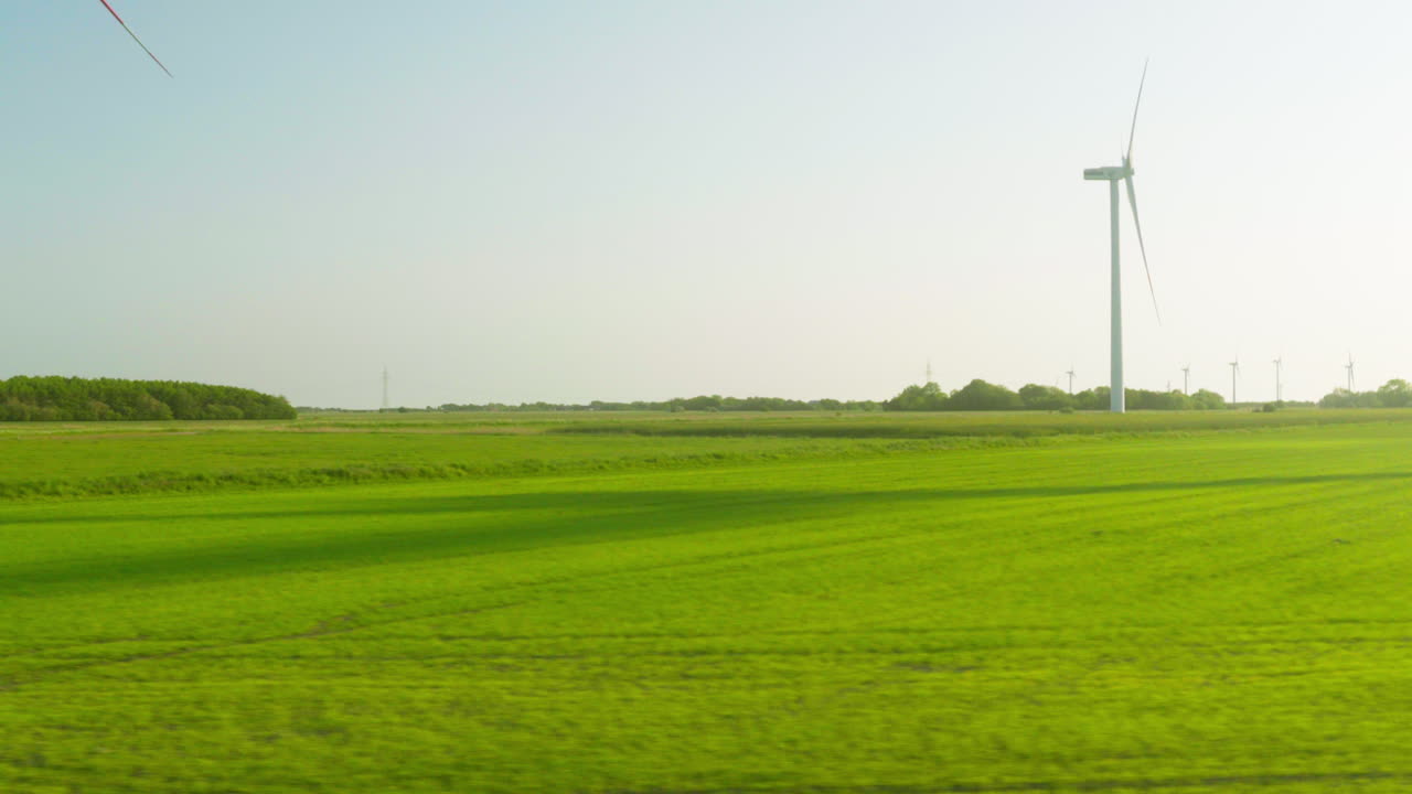 Sunlit Green Fields and Wind Turbines Passing By