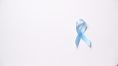 Detail-of-male-hand-placing-ribbon-in-light-blue-color-on-white-background