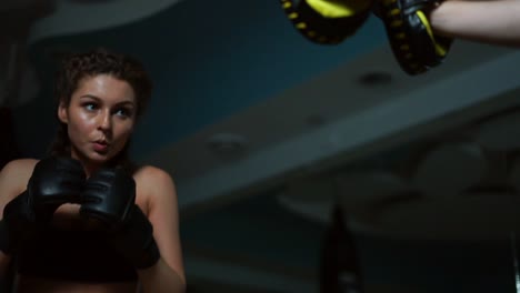 Close-Up-view-of-young-attractive-woman-in-boxing-gloves-training-with-her-couch-in-a-boxing-club.-Slow-motion-shot