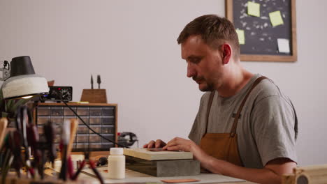 Bearded worker prepares leather sheet for processing in shop