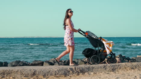 Long-hair-young-woman-walking-along-promenade-with-pram-in-summer-holiday.