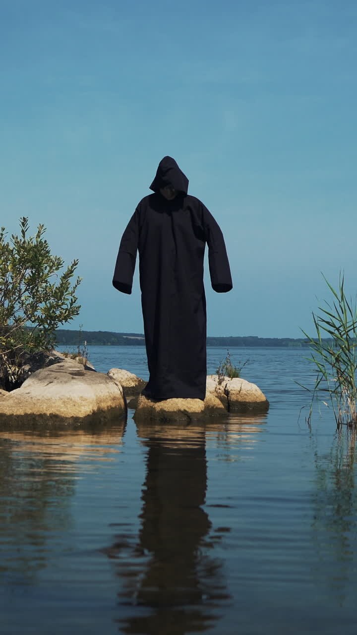 Demone terribile in piedi nel fiume. Figura spaventosa con mantello nero. Video verticale.