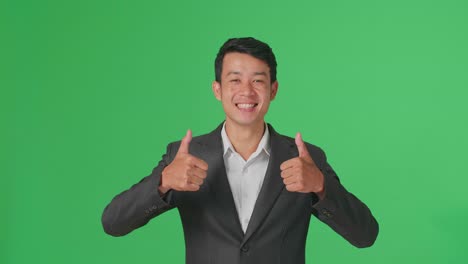 happy asian business man showing thumbs up gesture while standing in the green screen studio