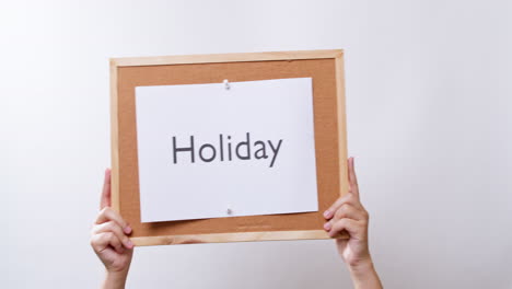 woman's hand shows the paper on board with the word holiday in white studio background with copy space