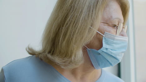 Close-up-shot-of-old-woman-in-medical-mask-looking-out-window