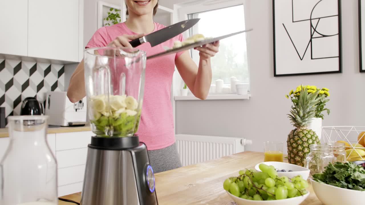 Giovane donna che prepara un frullato di frutta in cucina
