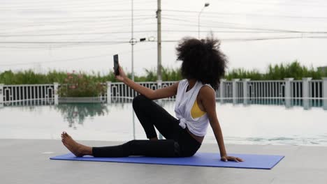 una mujer vestida para hacer ejercicio se sienta en una alfombra de yoga hablando por teléfono inteligente.