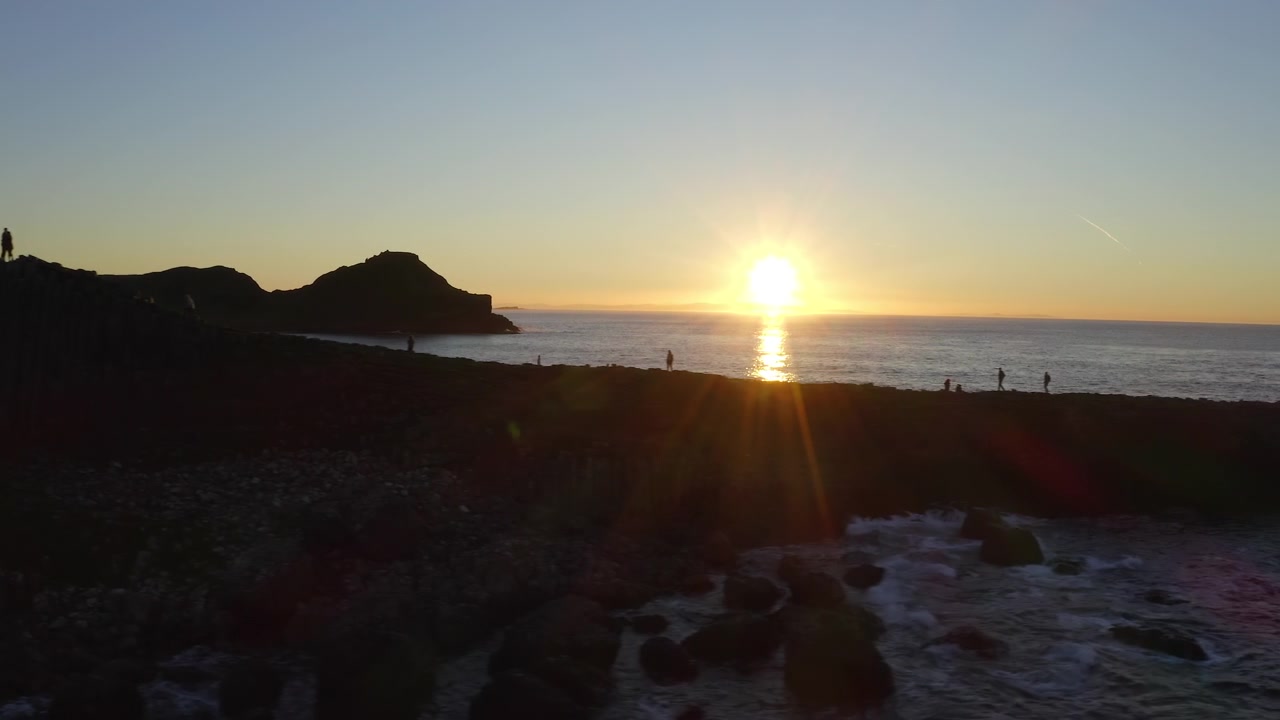 Hermoso atardecer en la Calzada del Gigante con turistas en silueta. Panorámica aérea hacia el mar.