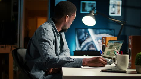 afroamericano freelance trabajando desde casa escribiendo notas e investigando