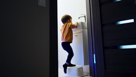 Little kid runs into the bathroom and stands on the prop. Toddler boy rejoices as he sees water flowing. Low angle view.