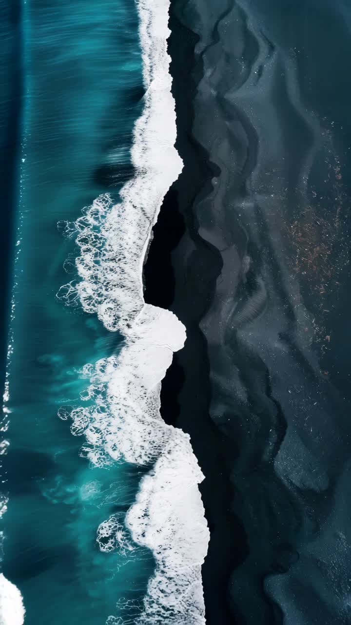 Vista aerea di onde che si infrangono su una spiaggia scura, che mostra uno straordinario contrasto di colori