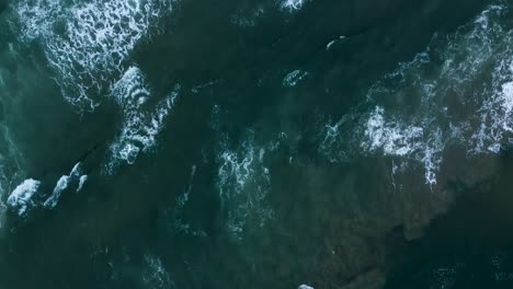 Aerial-top-down-shot-of-the-white-foamy-waters-of-the-Indian-Ocean-as-the-waves-and-strong-current-wash-up-onto-the-beautiful-beach-in-Sedgefield,-Western-Cape,-South-Africa