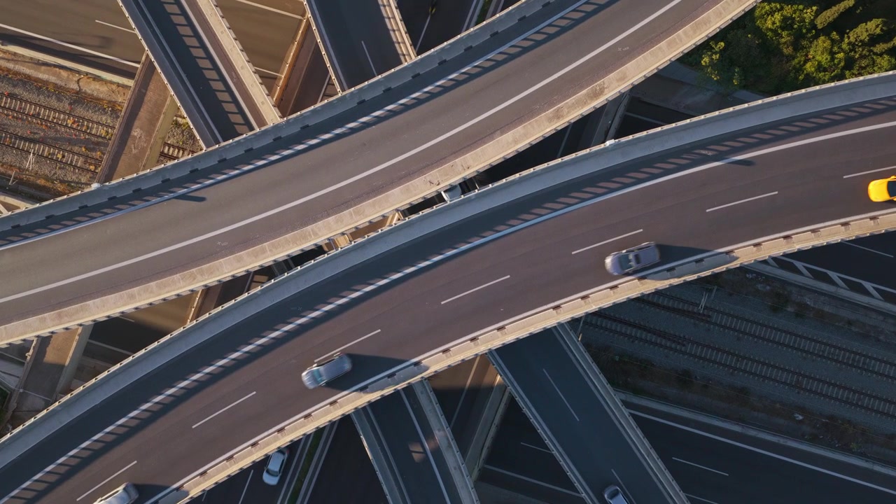 High angle top down view of a complex highway interchange with multiple overpasses and ramps showing cars and trucks driving through the road network during a sunny day