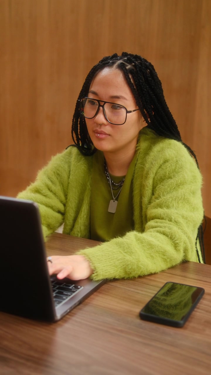 Focused Young Asian Woman Working on Laptop at Wooden Desk