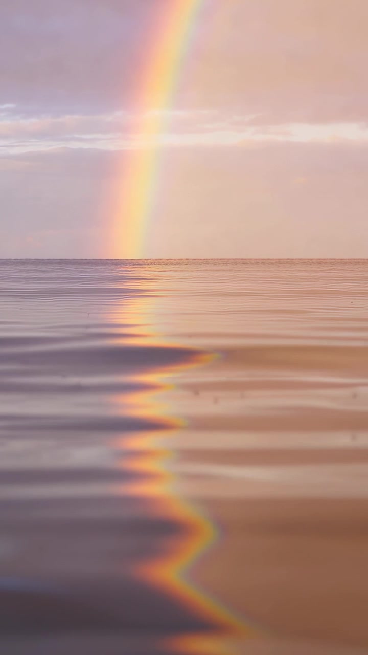 Vertical video: Forming vertical rainbow arc after rain, reflected band shimmering across calm sea