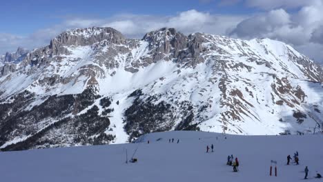 beautiful drone shot flying towards mountain range with people skiing down a piste in the italian alps